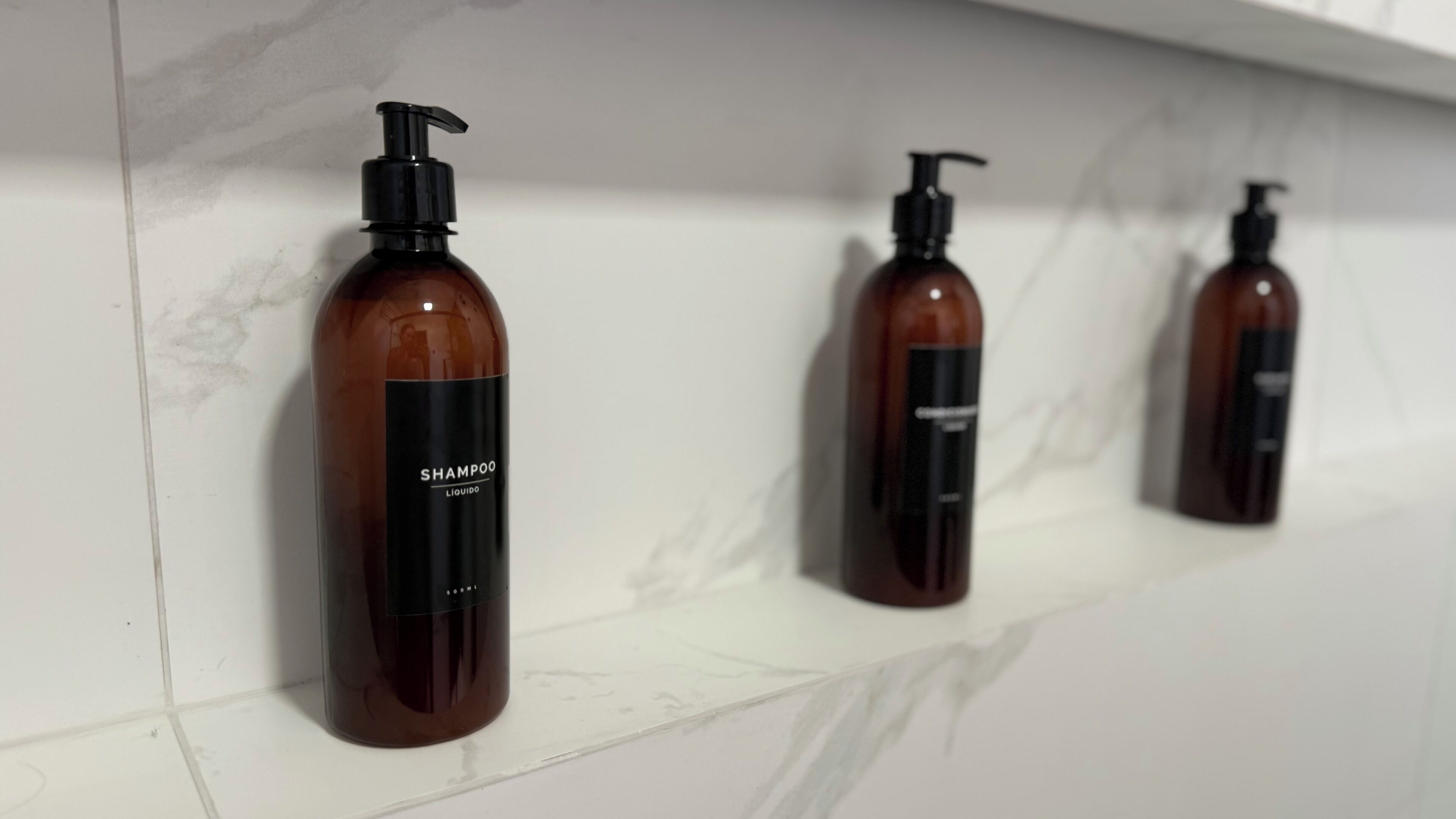 Three brown bottles with black pumps on a white tiled shelf.