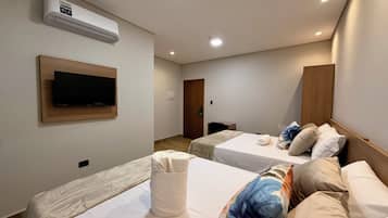 A hotel room with two single beds, a flat-screen TV mounted on the wall, and a wooden door.