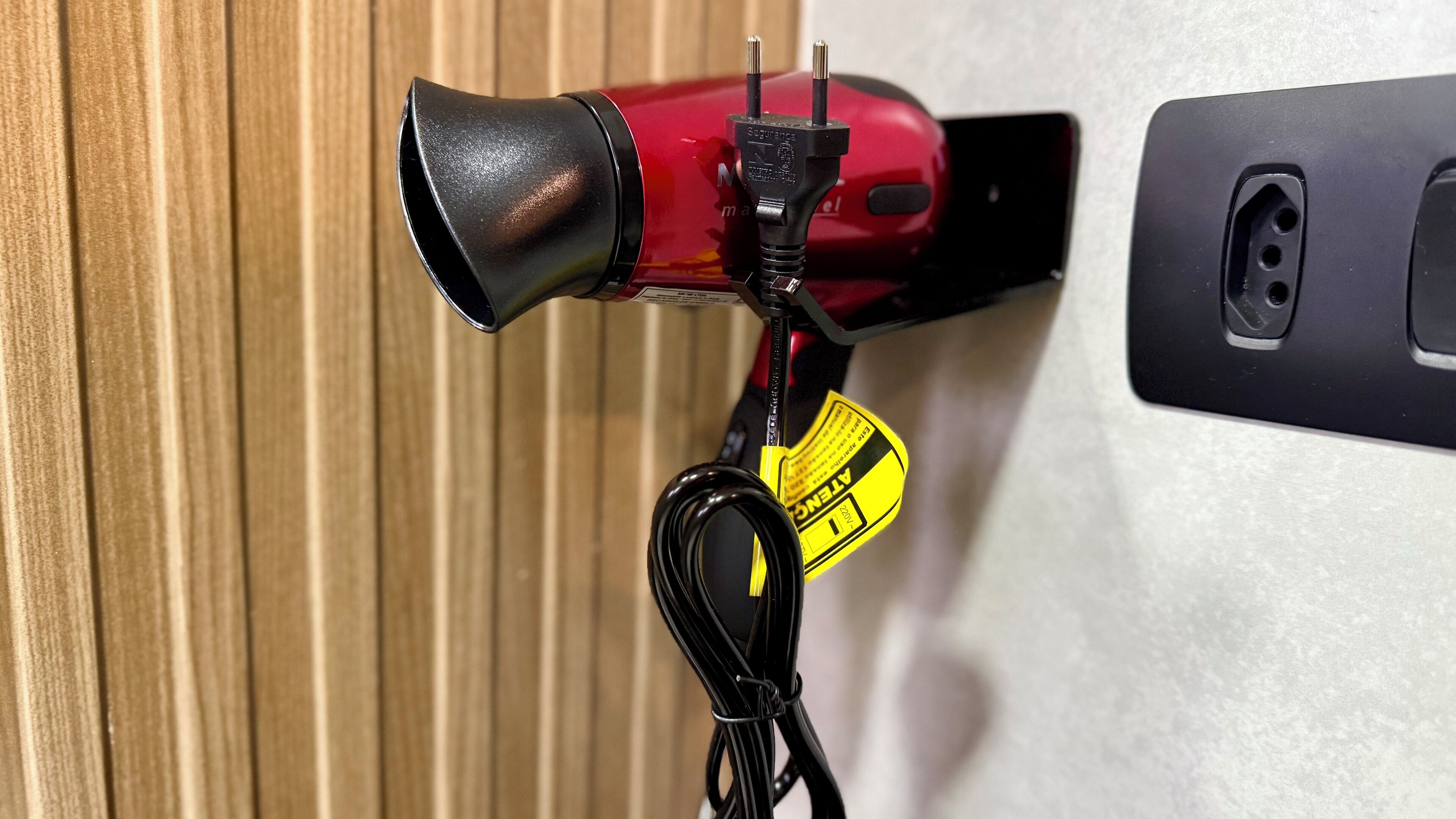 A red hairdryer with a black nozzle and a yellow tag attached to a black cord.