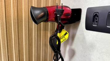 A red hairdryer with a black nozzle and a yellow tag attached to a black cord.