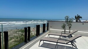 Varanda com vista para o oceano, com espreguiçadeiras e plantas em vasos.