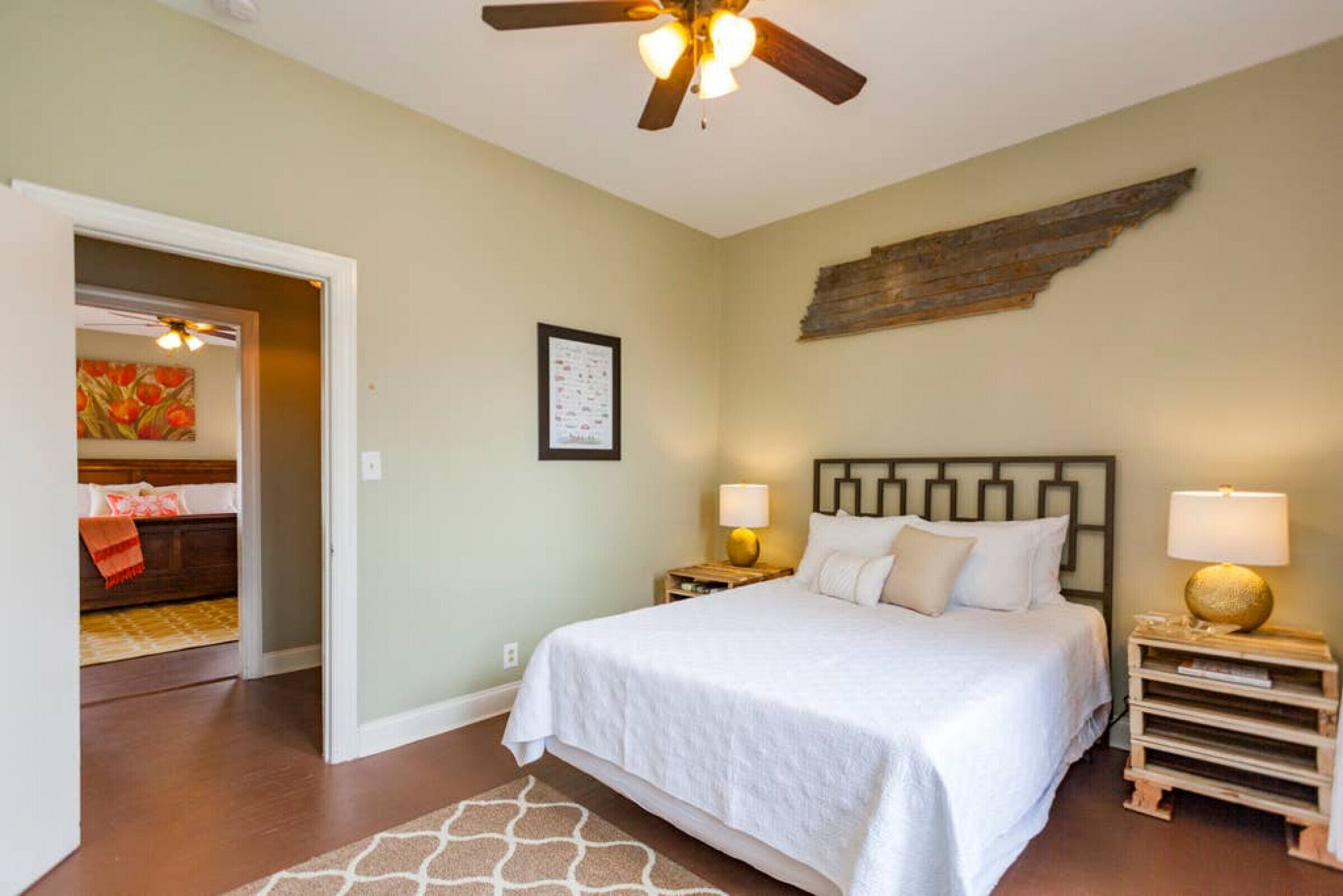 A bedroom with a bed, two bedside tables, a ceiling fan, and a wall-mounted artwork.