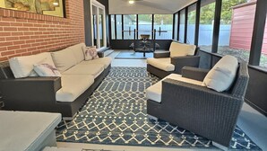 A covered patio area with a black and white patterned rug, a beige sofa, and a dark wicker chair. - Wonder Way: Sleeps 8! 4Bd/2Bth/Gym~Near NAS Jax~ (Jacksonville)