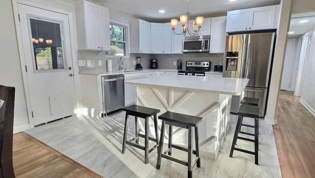 A modern kitchen with white cabinetry, a central island with stools, stainless steel appliances, and a chandelier. - Wonder Way: Sleeps 8! 4Bd/2Bth/Gym~Near NAS Jax~ (Jacksonville)