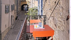Una calle estrecha flanqueada por edificios, un muro de piedra a la derecha y una pequeña mesa con un letrero al frente.