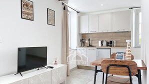 Una cocina moderna con armarios blancos, una mesa de comedor con sillas de madera, un televisor sobre un mueble de mármol y una isla de cocina.