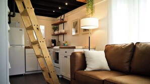 A kitchen with a wooden ladder, a brown leather sofa, and a floor lamp. - Downtown Caldwell Tiny Home - 1 mi UCA (Conway)