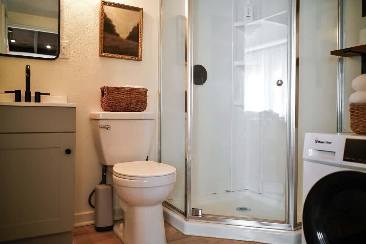 Een badkamer met toilet, een douche met glazen wand, een wasmachine en een lijst met een foto aan de muur.