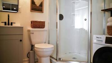 Een badkamer met toilet, een douche met glazen wand, een wasmachine en een lijst met een foto aan de muur.