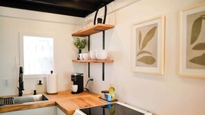 Une cuisine moderne équipée d’une cuisinière, d’un évier et d’un plan de travail en bois. Des étagères au-dessus du plan de travail servent à ranger des tasses et une plante.