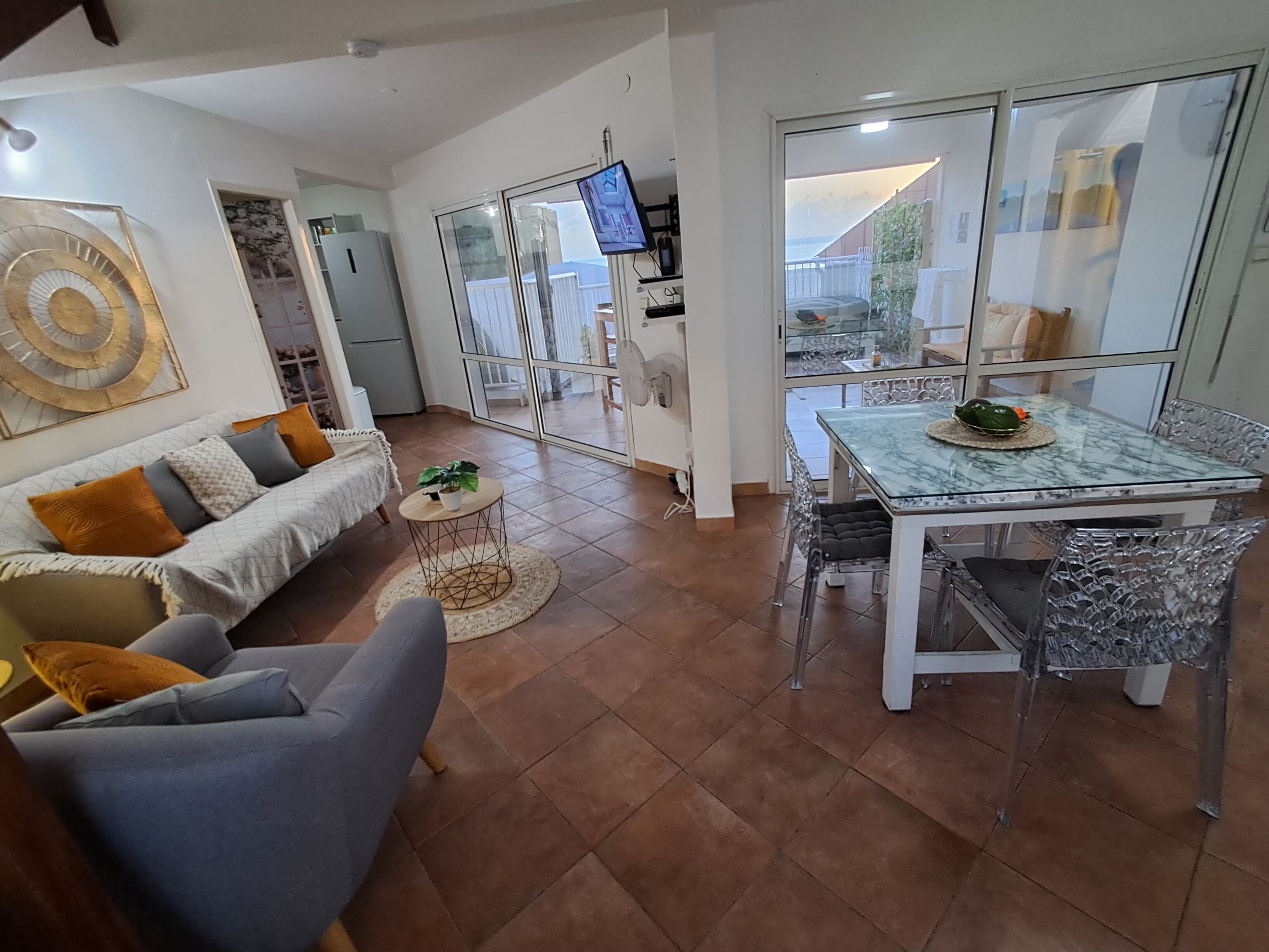 Una sala moderna con un sofá, una mesa de comedor con sillas, un televisor y vistas a través de amplios ventanales.
