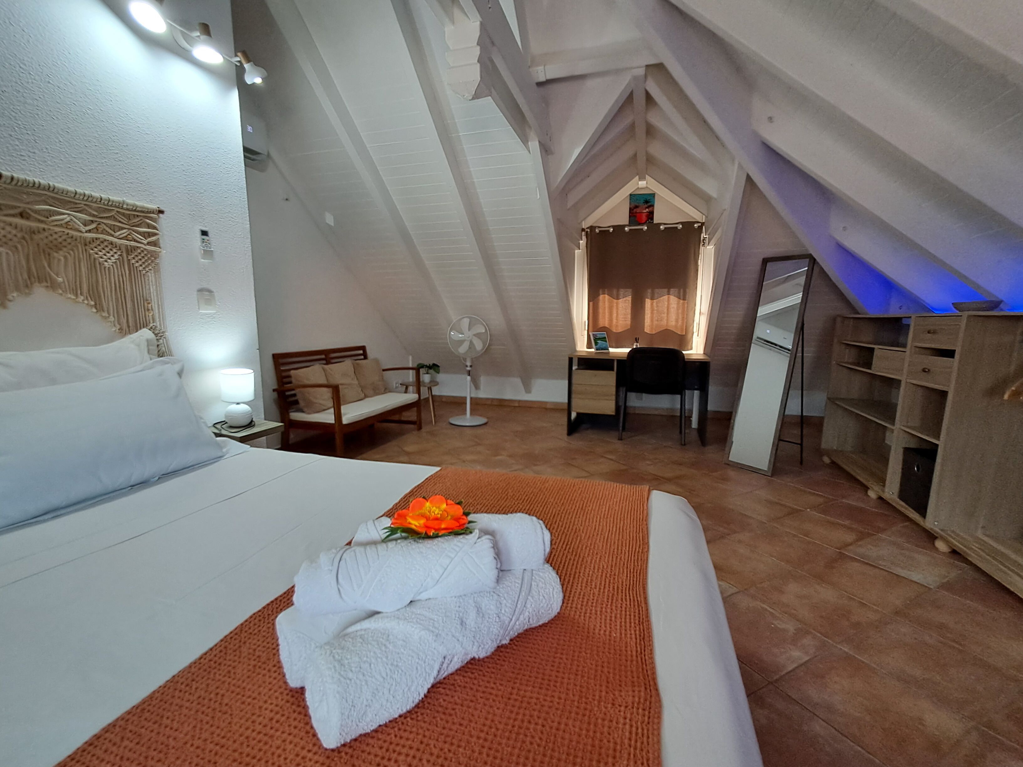 Une pièce confortable avec un lit, un bureau, une chaise et un ventilateur.
