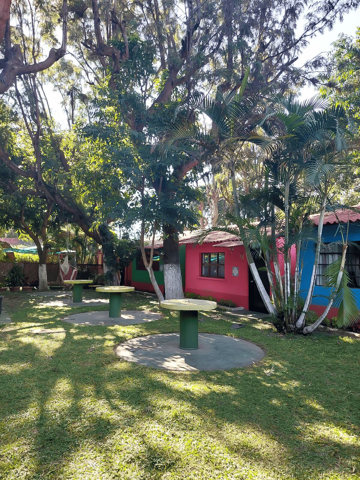 Un parque con mesas de picnic, un edificio rojo y abundante vegetación.