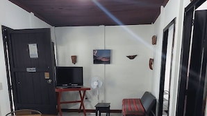 A dining area with a round table and chairs, a television on a stand, a fan, and a sofa. - El Aguacatal (Panajachel)