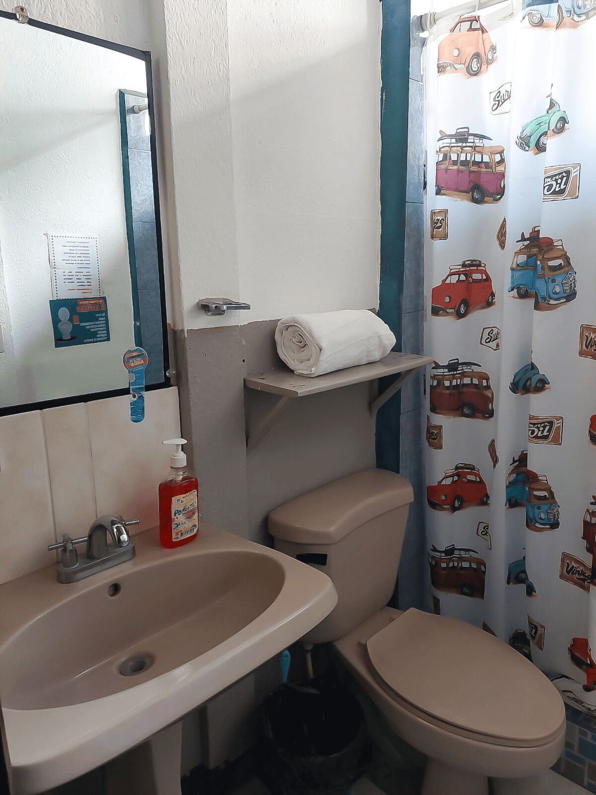 A bathroom with a sink, toilet, and a mirror. There is a towel on the toilet lid and a soap dispenser on the sink.