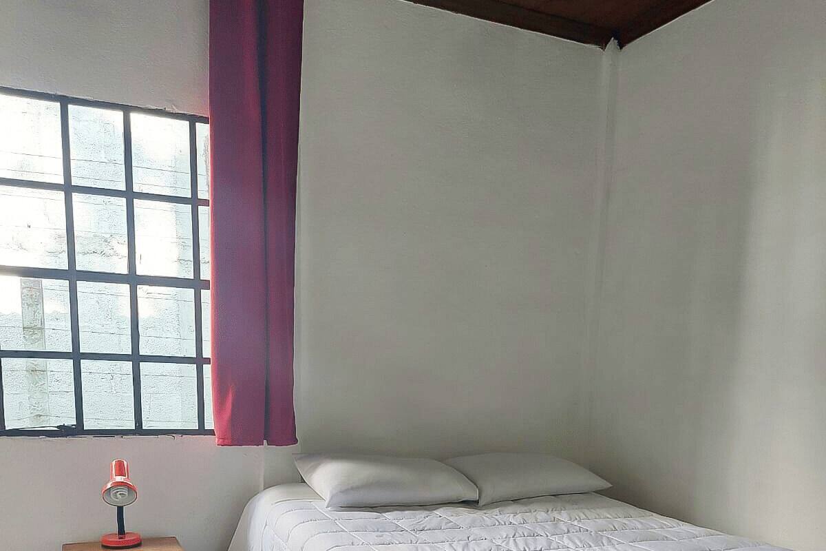 Une chambre à coucher avec un lit, une table de chevet, une fenêtre avec des rideaux et un plancher carrelé.
