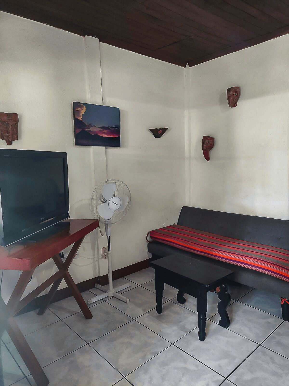 A living room with a TV, a fan, a sofa, and a small table.