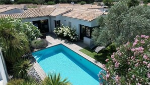 En moderne villa med swimmingpool, omgivet af frodigt grønt og et tegltag.