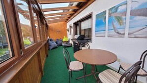 Un espace extérieur abrité, doté d’une pergola en bois, d’une table ronde avec des chaises et d’un barbecue.