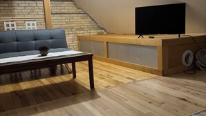 Ett rum i loftstil med trägolv, en grå soffa, ett soffbord, en tv på ett träställ och en mönstrad matta.