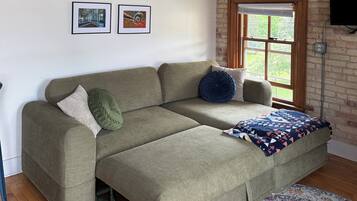 A room with a sofa, a patterned rug, a brick wall, and framed pictures on the wall.