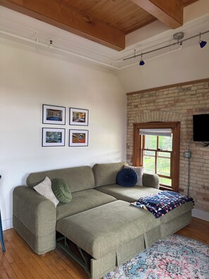 A room with a sofa, a patterned rug, a brick wall, and framed pictures on the wall. - Studio loft Grand Traverse Commons (Traverse City)