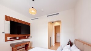 A modern hotel room with a large bed, a TV mounted on the wall, a wooden desk, and a walk-in closet. - Tropical Voyage 3BR Garden View (Rio Hato, Coclé)