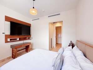 A modern hotel room with a large bed, a TV mounted on the wall, a wooden desk, and a walk-in closet. - Tropical Voyage 3BR Garden View (Rio Hato, Coclé)