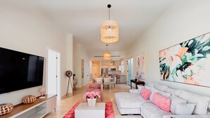 A modern living room with a flat-screen TV, a white sofa, a red rug, and a large abstract painting. - Tropical Voyage 3BR Garden View (Rio Hato, Coclé)