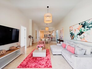 A modern living room with a flat-screen TV, a white sofa, a red rug, and a large abstract painting. - Tropical Voyage 3BR Garden View (Rio Hato, Coclé)