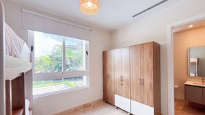 A modern room with a large wardrobe, a window with a view of greenery, and a bathroom with a mirror and sink. - Tropical Voyage 3BR Garden View (Rio Hato, Coclé)