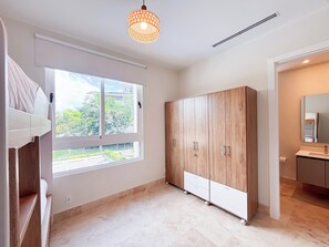A modern room with a large wardrobe, a window with a view of greenery, and a bathroom with a mirror and sink. - Tropical Voyage 3BR Garden View (Rio Hato, Coclé)