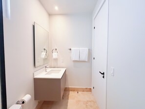 Een kleine, schone badkamer met een wit wastafelmeubel, spiegel en handdoekhouder.