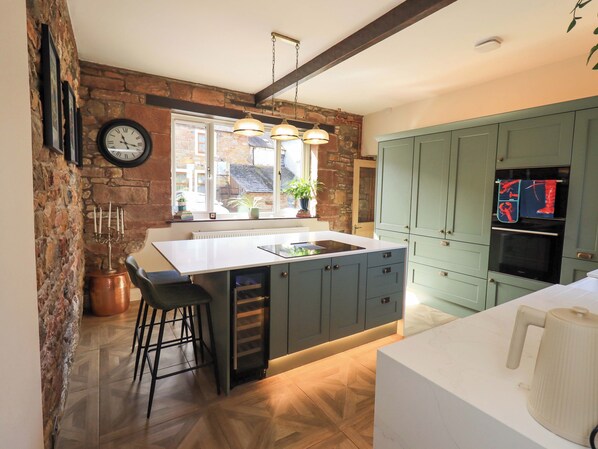 A kitchen with a central island, bar stools, a clock, and a view of the outside.
