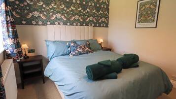 A bedroom with a floral wallpaper, a bed with blue bedding, two bedside tables with lamps, and a framed picture on the wall.