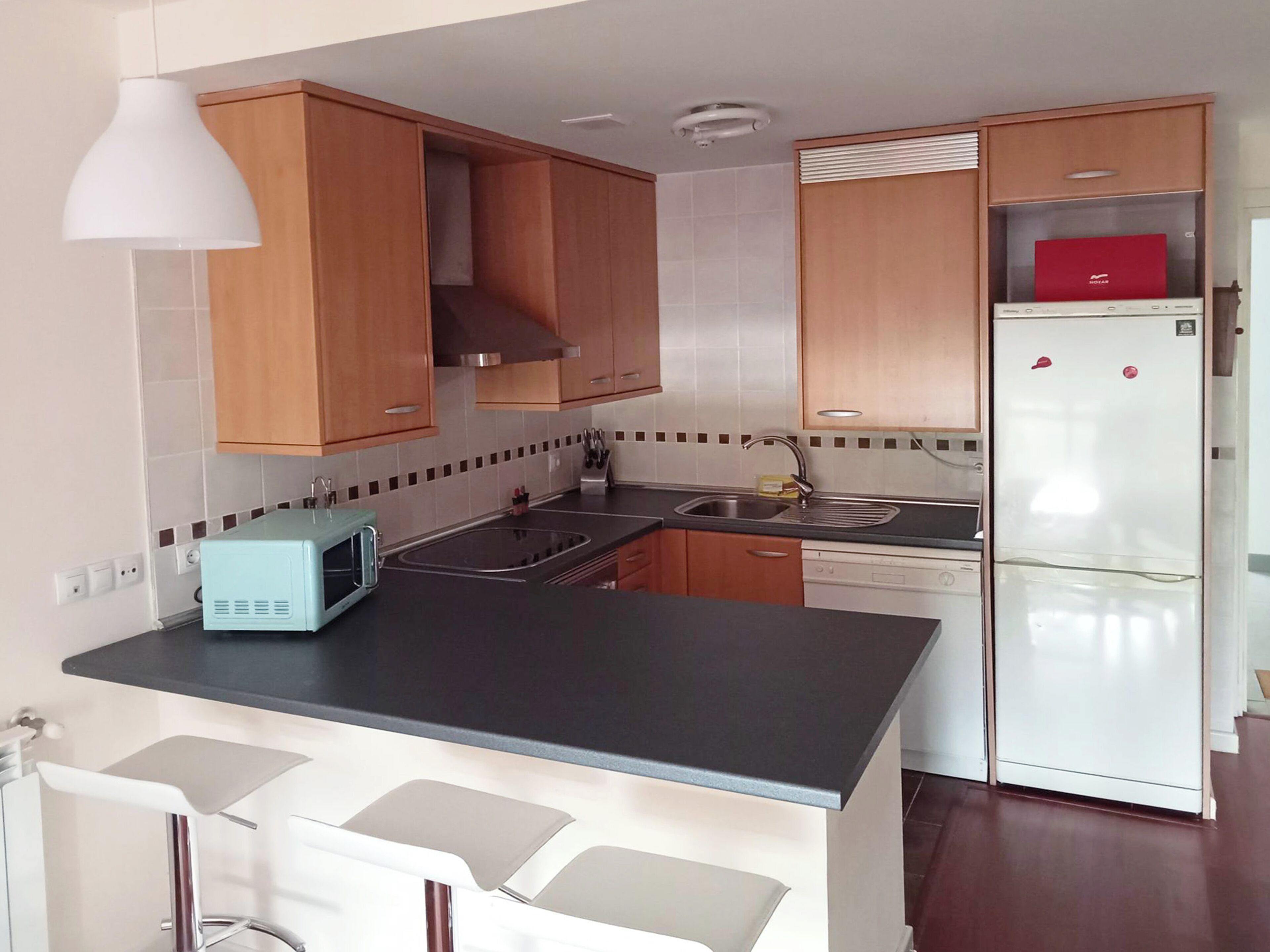 A modern kitchen with wooden cabinets, a black countertop, a white refrigerator, and a microwave.