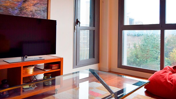 A modern living room with a glass coffee table, a flat-screen TV on an orange stand, and a red bean bag. - Apartamentos Las Margas Sabiñanigo 3000 (Sabiñánigo)