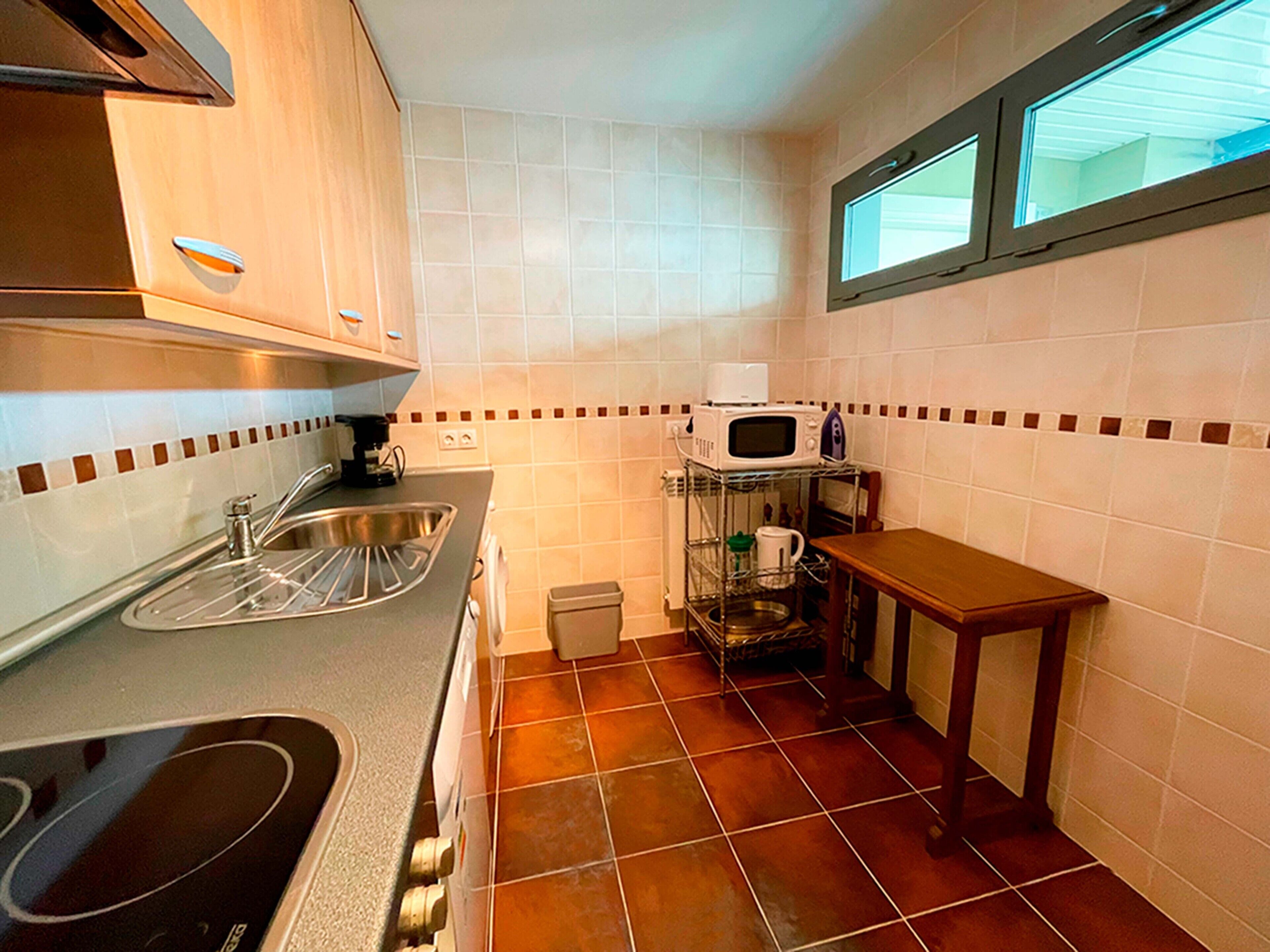 Una cocina compacta con lavamanos, estufa, microondas y una pequeña mesa.