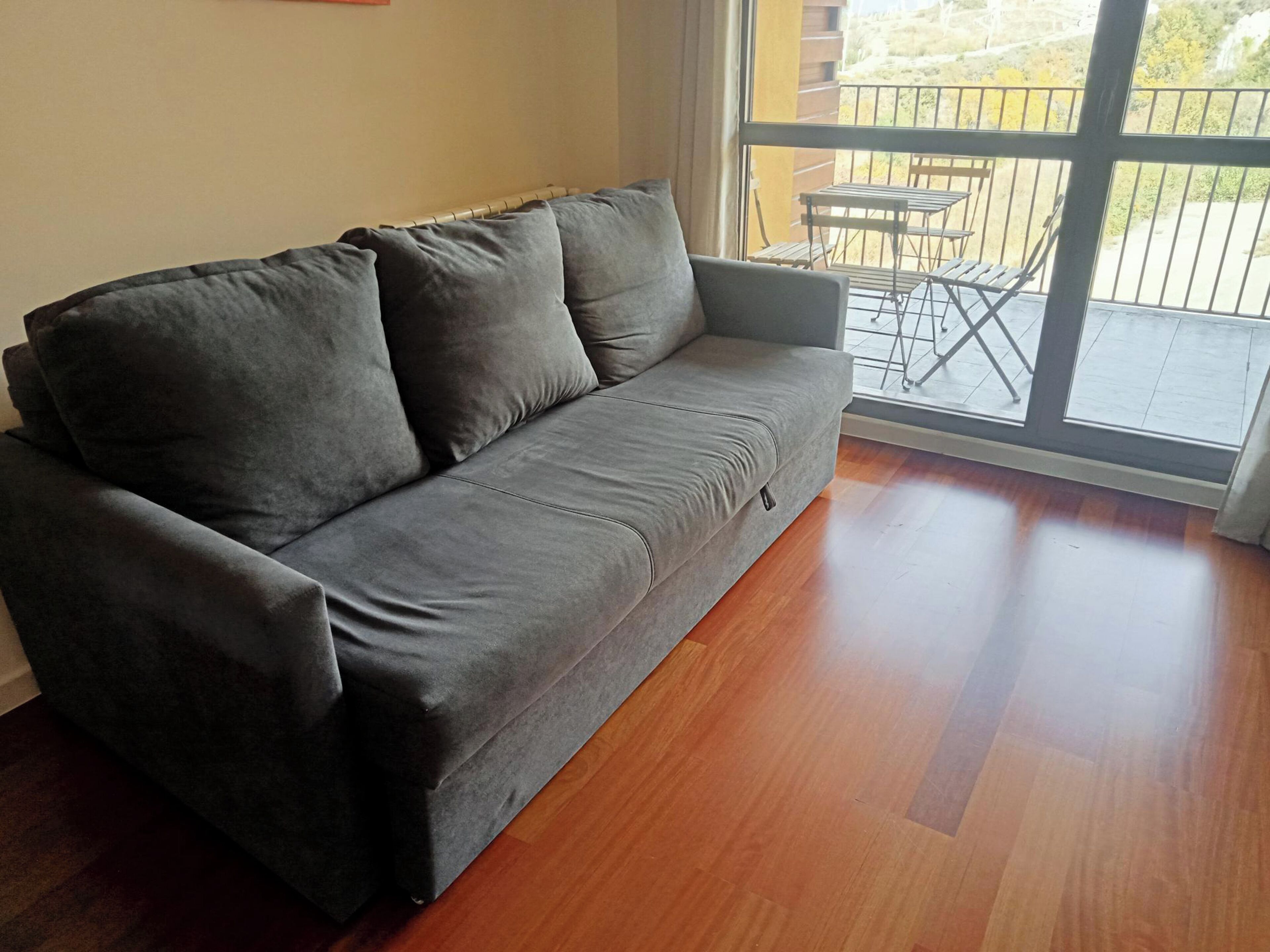 Un canapé gris doté d’une petite poche à fermeture éclair, placé à côté d’une porte-fenêtre coulissante donnant sur un espace patio extérieur avec une table et des chaises.