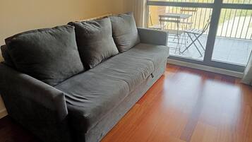 Un canapé gris doté d’une petite poche à fermeture éclair, placé à côté d’une porte-fenêtre coulissante donnant sur un espace patio extérieur avec une table et des chaises.