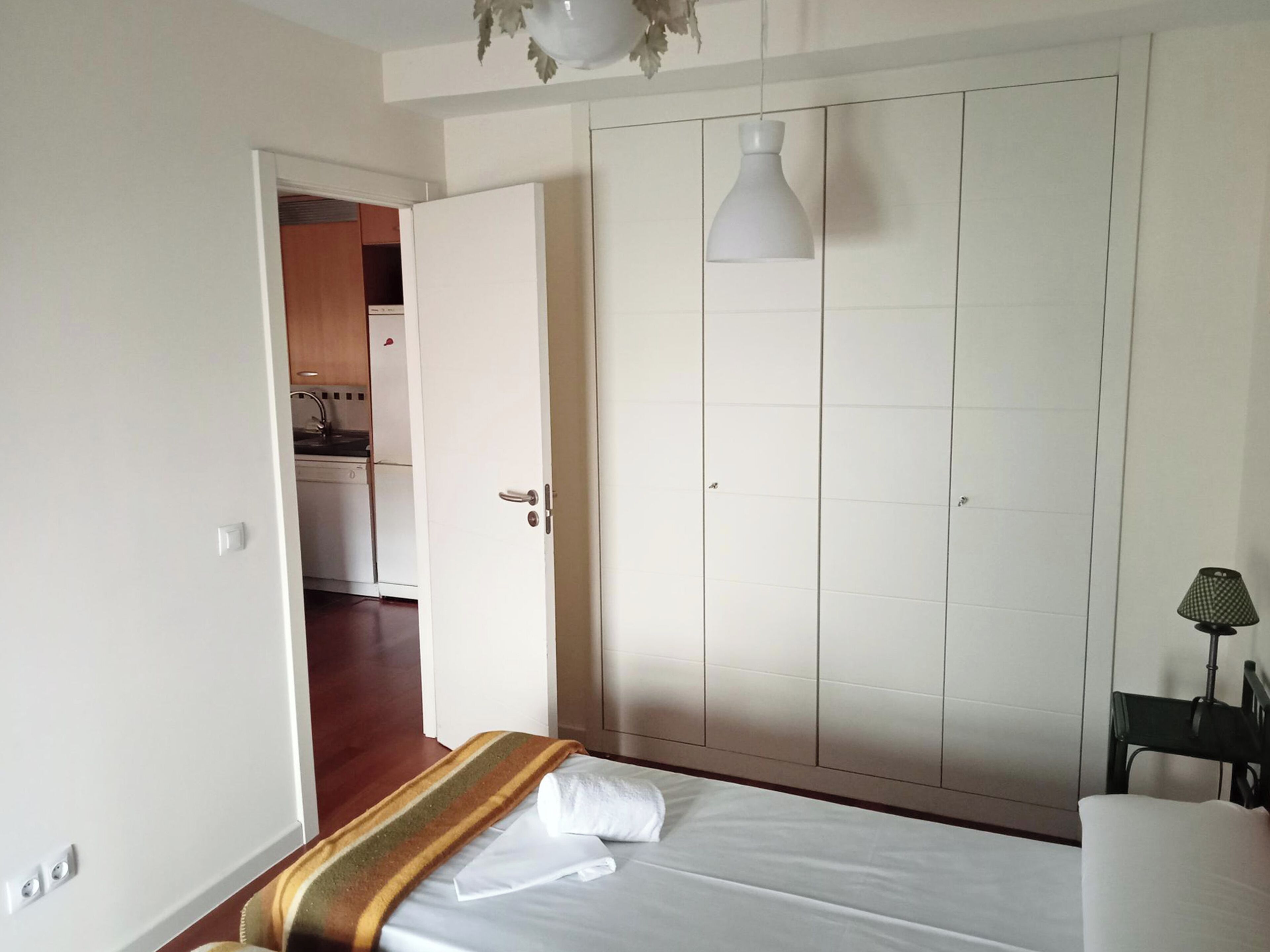 Et soveværelse med seng, garderobe og et lille bord med lampe.