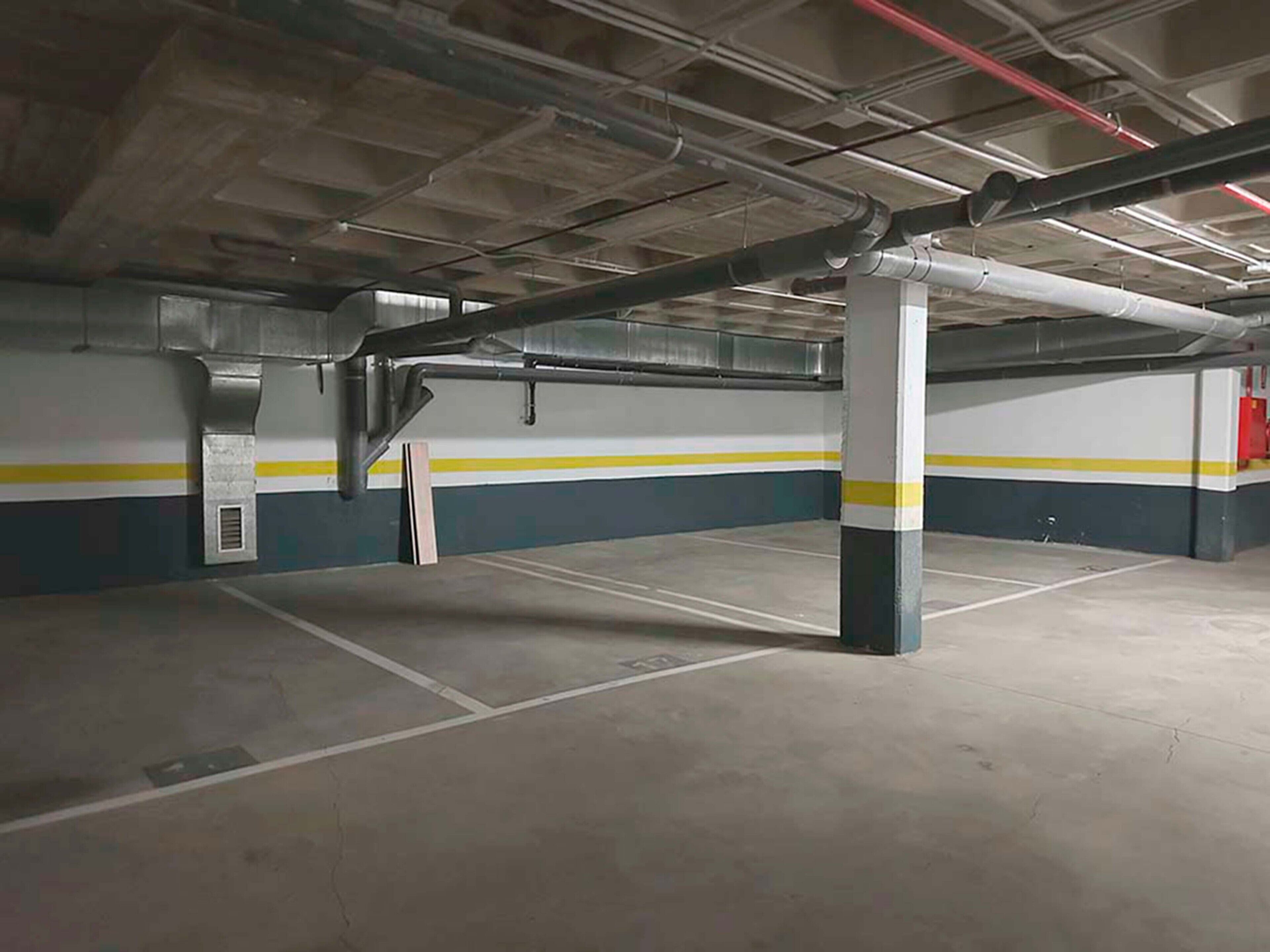 An empty parking garage with concrete floors and walls, featuring yellow and blue stripes, and visible structural elements like columns and pipes.