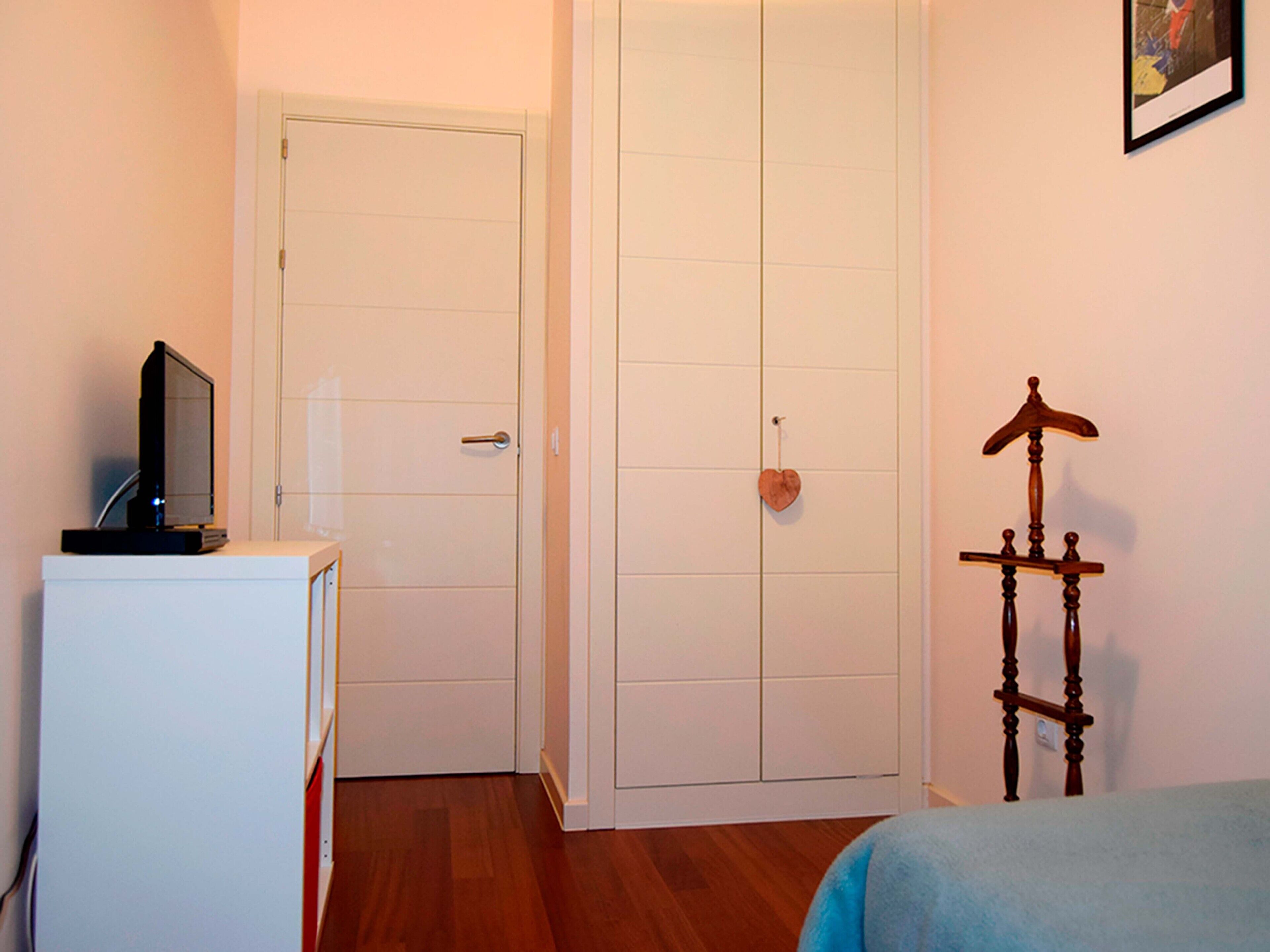A bedroom with a bed, a desk with a computer, a wardrobe, and a wooden chair.