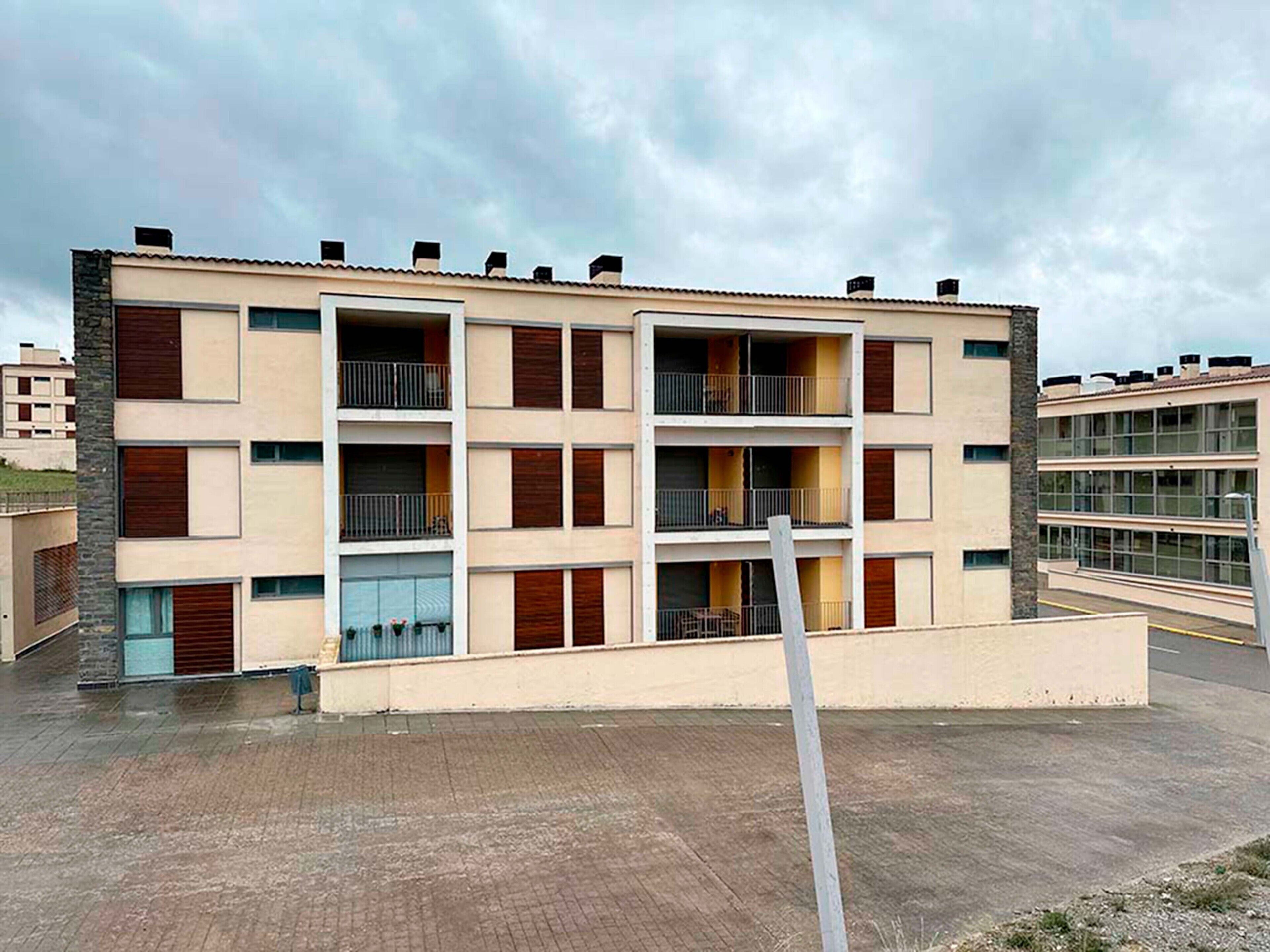 Un edificio residencial de varios pisos con balcones, techo plano y un área pavimentada.