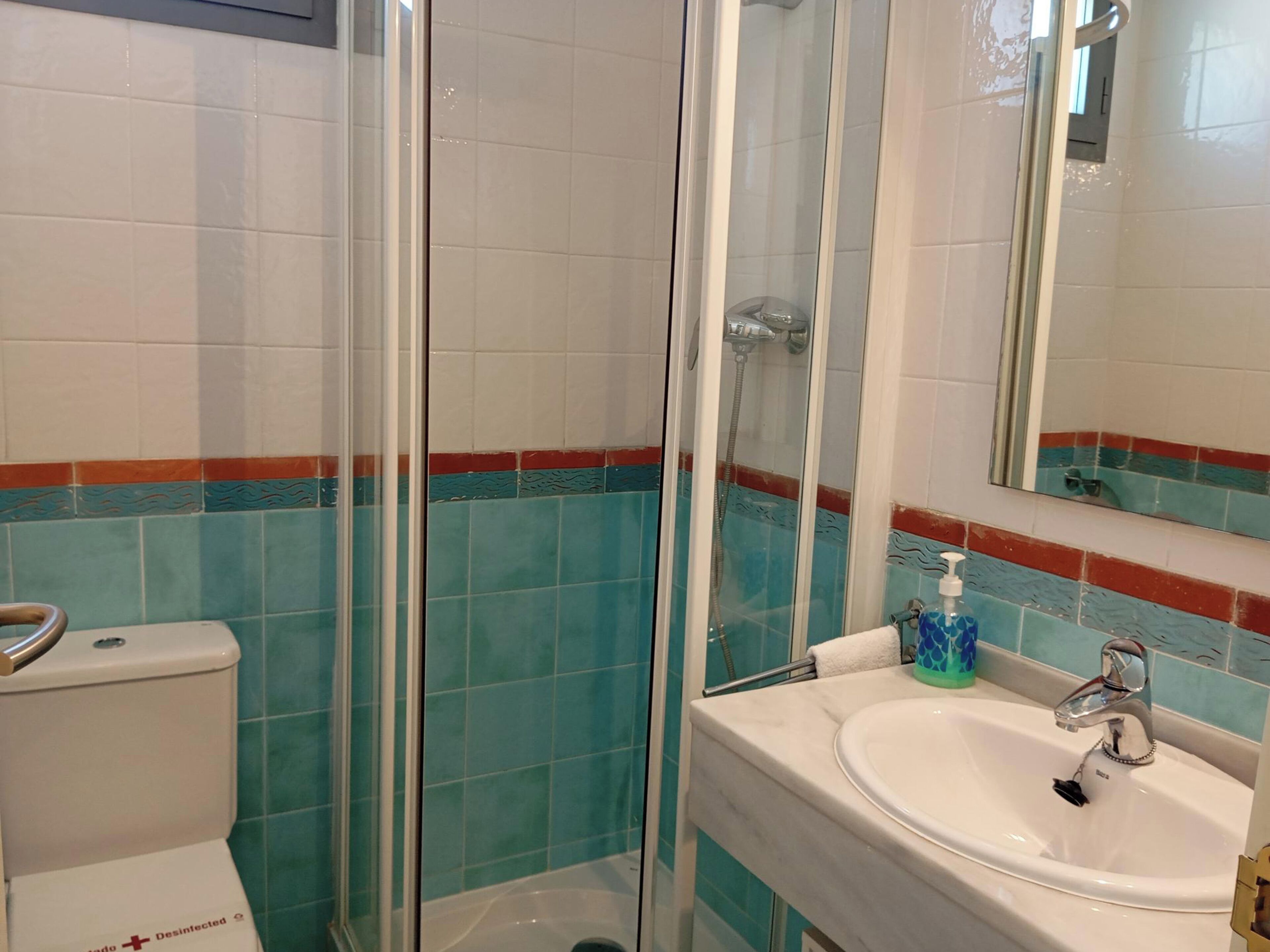 A bathroom with a toilet, a glass-enclosed shower, and a sink with a mirror.