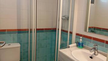 A bathroom with a toilet, a glass-enclosed shower, and a sink with a mirror.