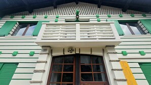 A building with a white facade, green window shutters, and a central balcony with a metal railing. - Rifugio TEA Dolomiti (Canale d'Agordo)