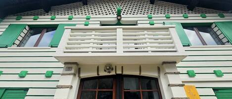 A building with a white facade, green window shutters, and a central balcony with a metal railing.