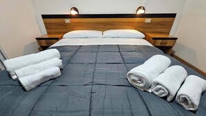 A neatly made bed with a dark grey duvet, two bedside tables with lamps, and rolled white towels on the bed. - Rifugio TEA Dolomiti (Canale d'Agordo)