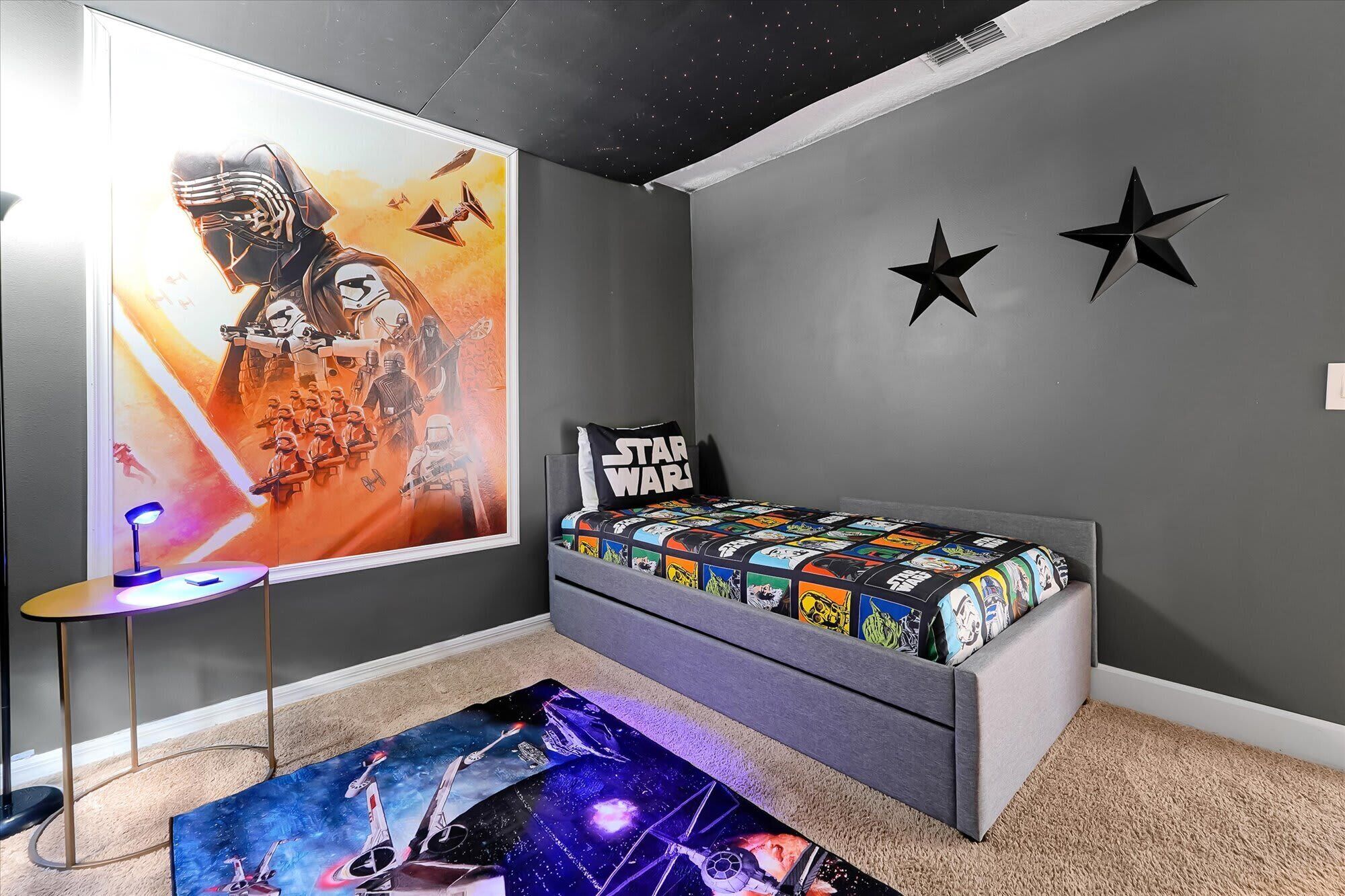 A bedroom with a Star Wars themed bedspread, a Star Wars poster on the wall, and a Star Wars themed rug.
